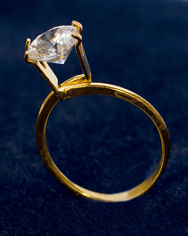 Small gold-tone display ring holding a single clear stone for photography and jewelry display purposes