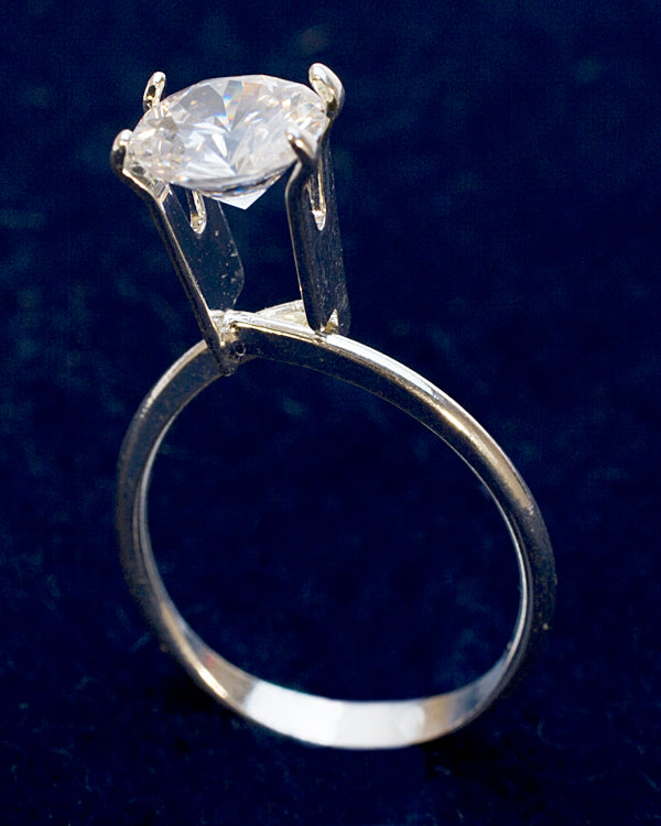 Large silver-tone display ring showcasing a clear stone with secure prongs on a dark background