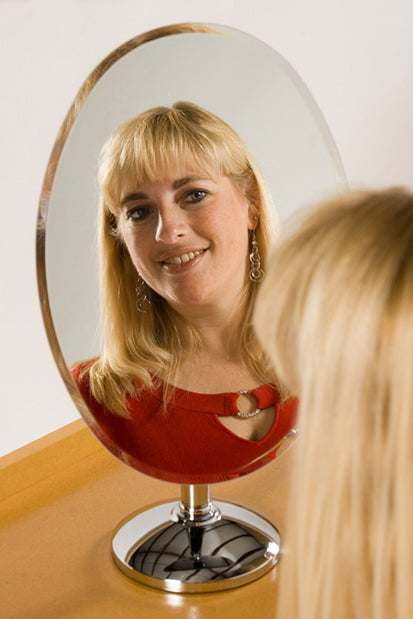 18" rimless chrome pedestal oval mirror on countertop reflecting woman with blonde hair